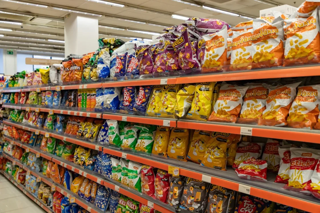 Fully stocked supermarket shelving with colorful snack chip packages in bulk, showcasing wholesale food distribution and retail merchandising for foodservice suppliers.