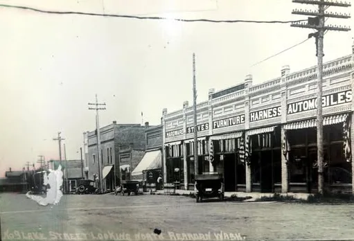 Vintage early 20th century wholesale food supplier warehouse with large storefront displaying furniture and automotive supplies signage, featuring period commercial architecture.